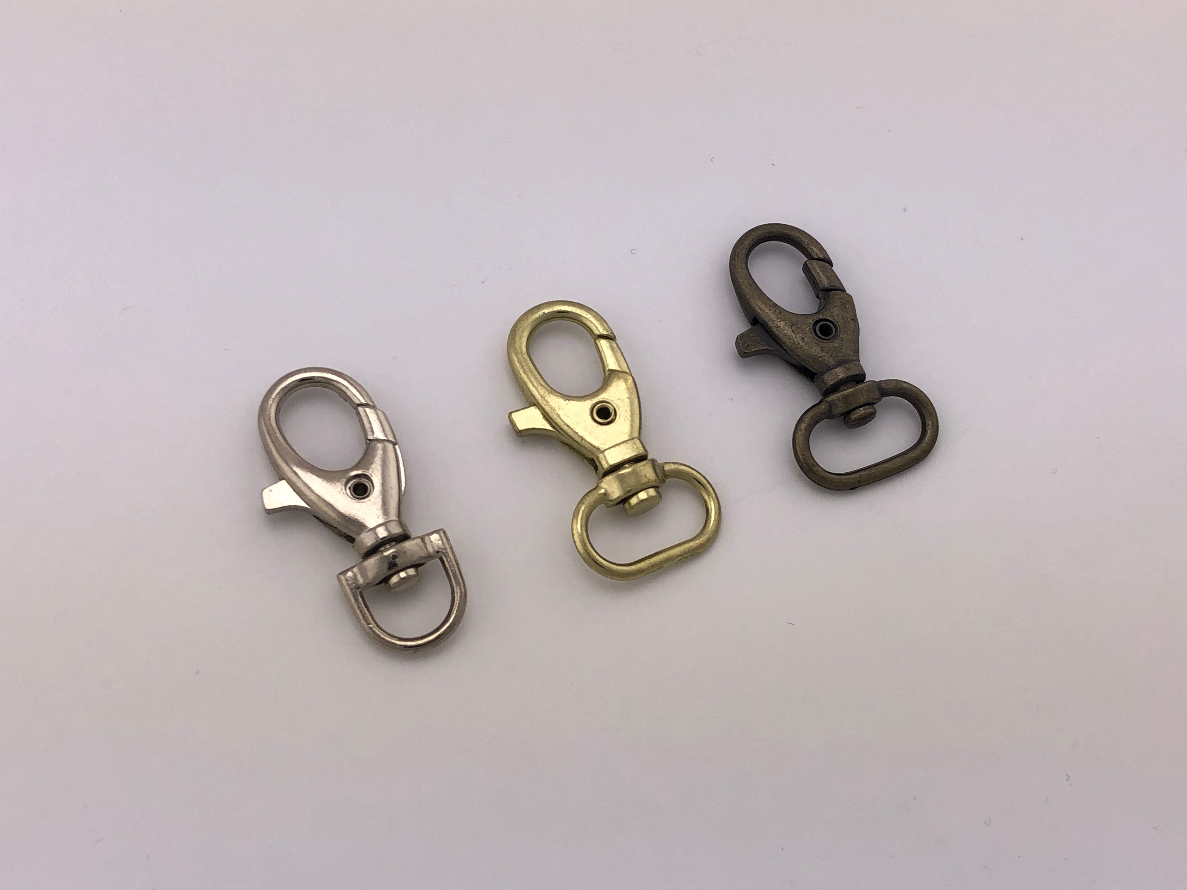 Pack de 100 piezas de Bandola metálica fundida con argolla giratoria para gafete o llavero de 40 mm, en diferentes acabados como nickel, latón y oro viejo. Pack de 100 piezas de Bandola metálica fundida con argolla giratoria para gafete o llavero de 40 mm, en diferentes acabados como nickel, latón y oro viejo.